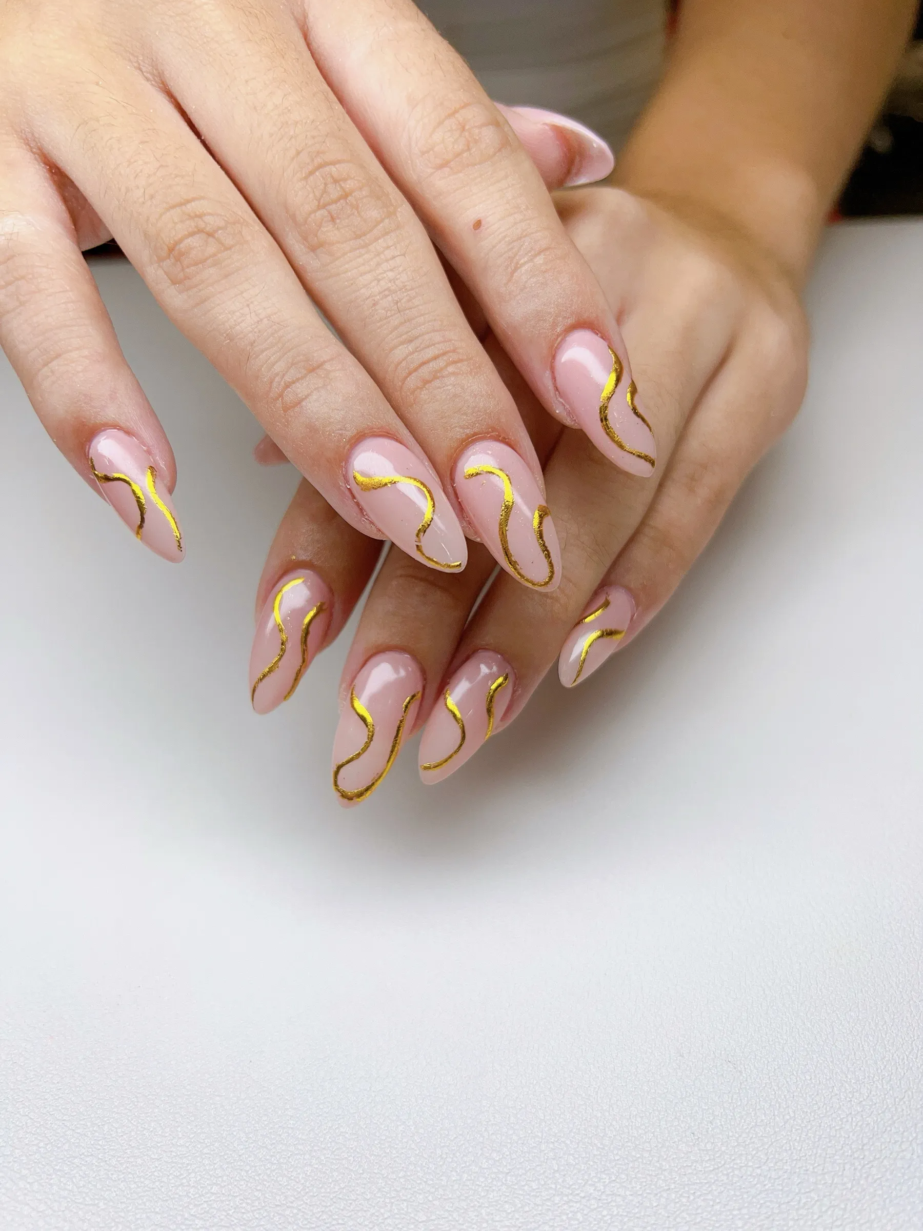 Nude almond nails with hand painted gold swirl line nail art on every finger